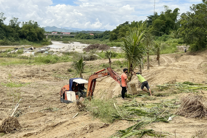 Máy múc san ủi đất do UBND xã Diên Đồng quản lý và ông Hưởng (đứng phía dưới) cầm gậy để cản trở người dân khi họ nhổ cọc cắm mốc (ảnh nhỏ).